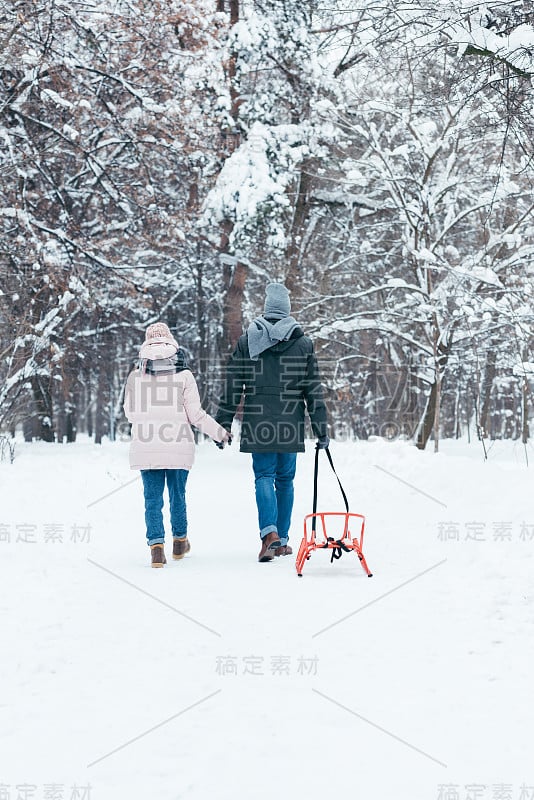 后视图的夫妇拉着雪橇在雪山公园散步