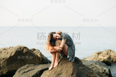 一个年轻美丽的女孩穿着大石头，风景如画的海边