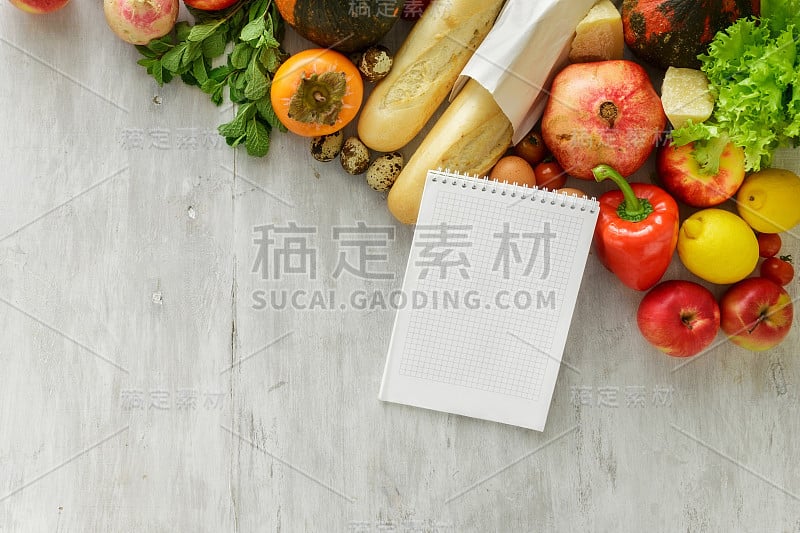 顶视图一套生的食物与笔记本在白色木制的背景。健康食品的概念