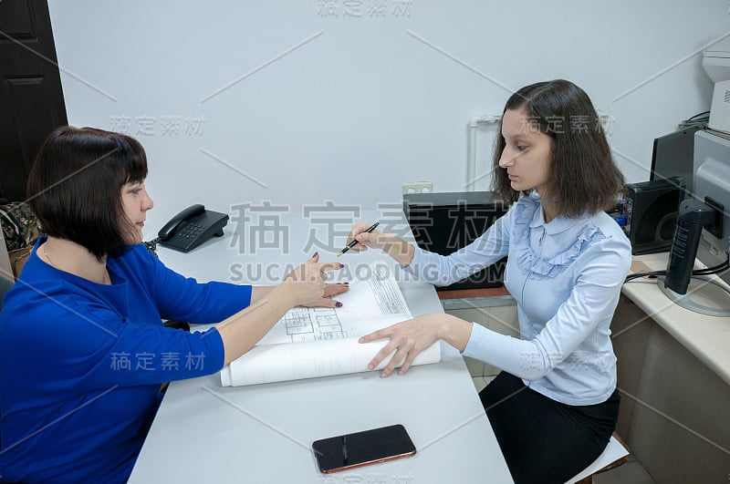 一个穿蓝衣服的女人递给那个女孩一支笔，让她在办公室的图纸上签字