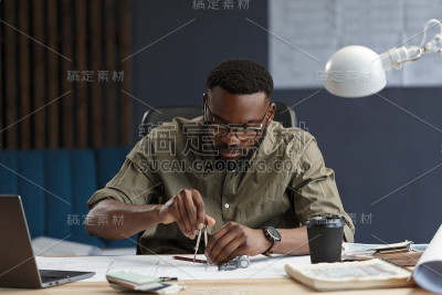 非裔美国建筑师在办公室里设计蓝图。工程师检查建筑平面图，为建筑工程画草图。黑人英俊男子坐在工作场所的