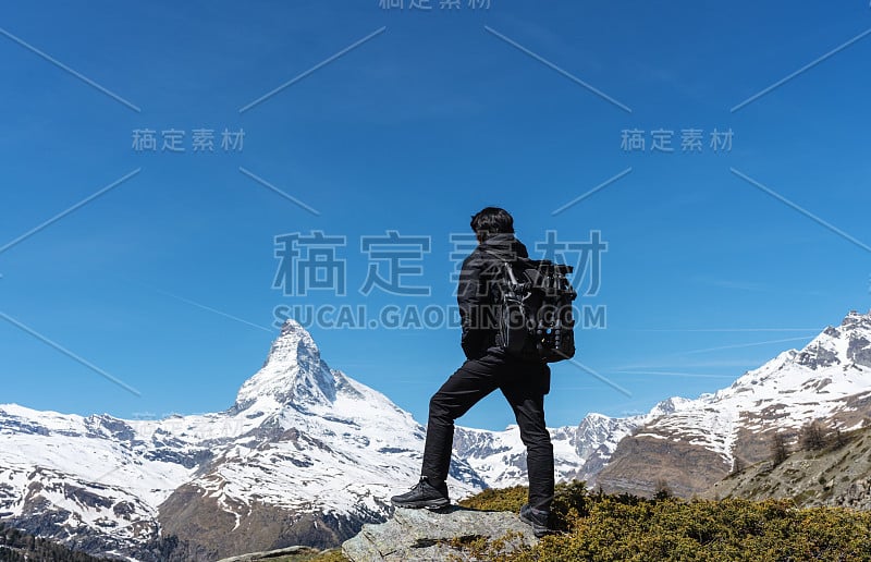 在瑞士旅行时，一名男子背着背包站在岩石上观看马特洪山景。在瑞士泽马特徒步旅行