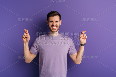 兴奋的年轻人双手交叉，闭着眼睛站在紫色的背景上