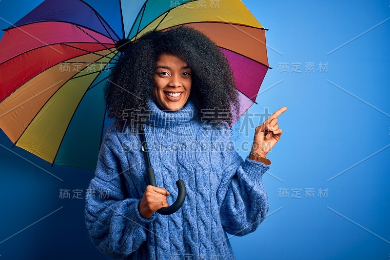 年轻的非洲裔美国妇女与非洲式的头发下彩色伞为冬天的天气下雨非常高兴指着与手和手指的一边