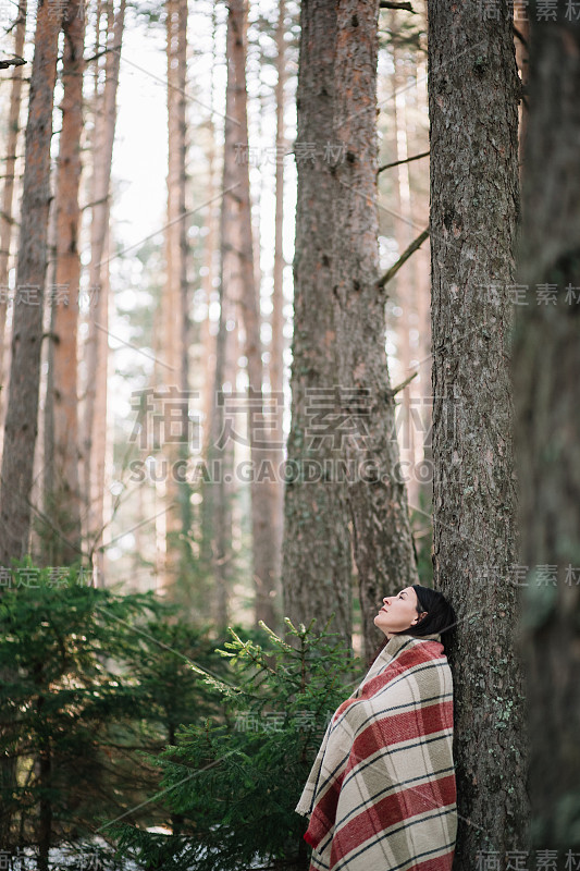 寒冷的女人在树林里用被子取暖