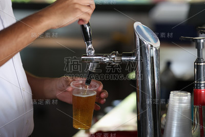 调酒师将冰冻的啤酒从机器中倒入玻璃杯。