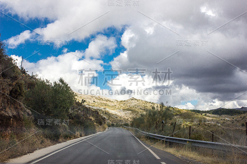 孤独而阴沉的路，有云，有有趣的光。充满戏剧性色彩的山路。旅行、户外、旅行的概念。