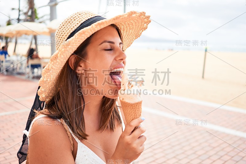 年轻漂亮的女人在一个阳光明媚的夏日假日在海滩上吃冰淇淋