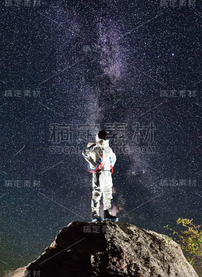 在星空下，宇航员站在岩石山上。