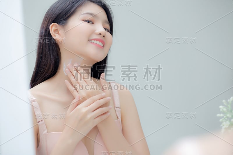 美丽性感的年轻亚洲女人看着镜子，在颈部和信息上应用霜，美丽的女孩应用身体乳液皮肤保健和柔软的水，治疗