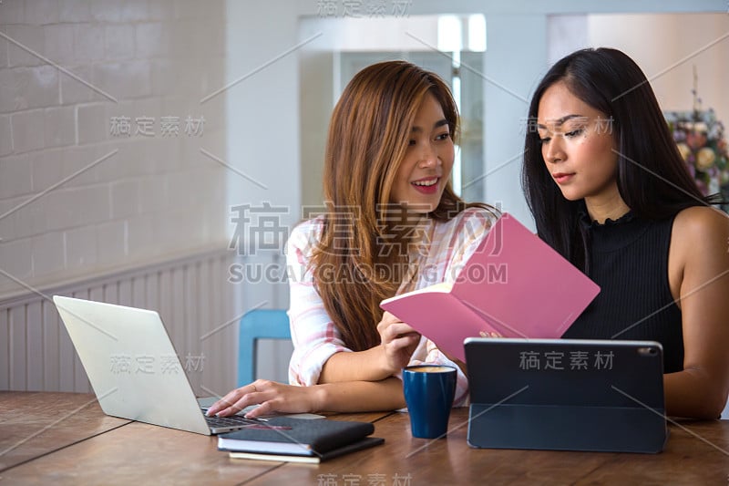 两个漂亮的亚洲学生正在使用电脑和课本。在家里用温暖的光线复习功课