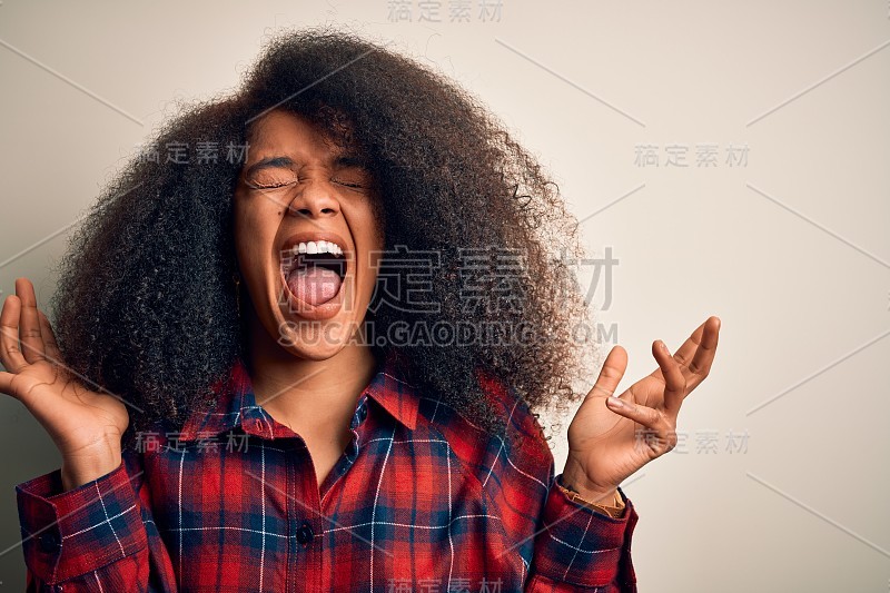 年轻美丽的非洲裔美国女人穿着休闲衬衫，在孤立的背景下，高举双臂，闭上眼睛，兴奋地尖叫着，为成功而疯狂