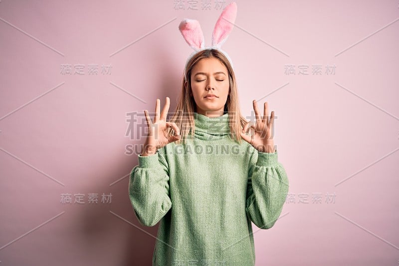 年轻美丽的女人戴复活节兔子耳朵站在孤立的粉红色背景放松和微笑与眼睛关闭做冥想手势与手指。瑜伽的概念。