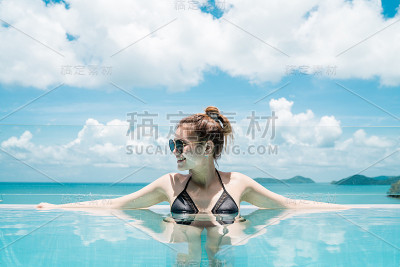 肖像女人放松豪华泳池别墅，无限海景，她戴墨镜，拷贝空间。