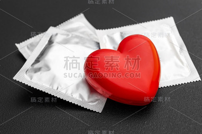 黑色背景上的红心和避孕套。安全性行为的概念。