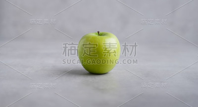 在灰色背景下分离的新鲜的单一绿苹果。