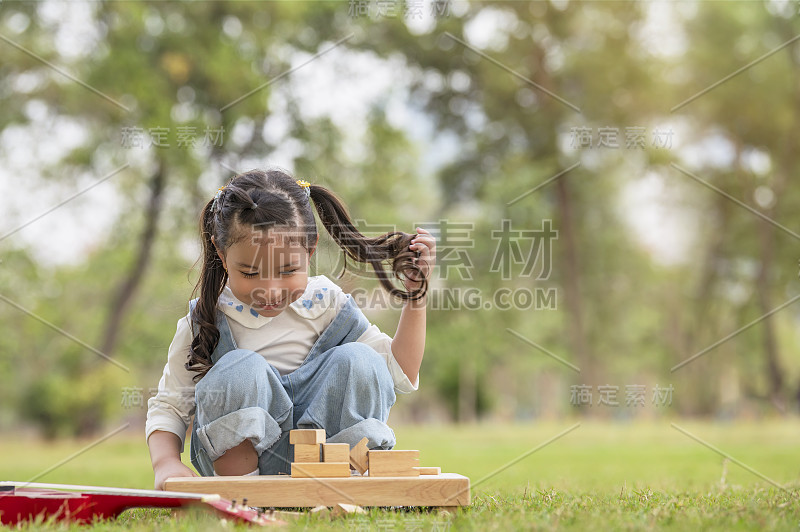 可爱的
一个小女孩坐在草地上玩一种有趣的游戏活动，包括积木和砖块。
爱好的概念