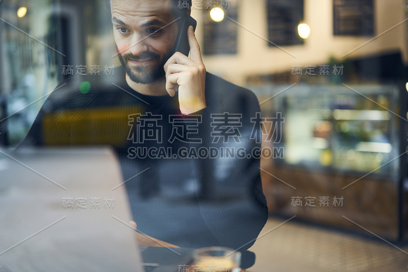 裁剪的图像，惊讶的年轻胡子男子通过现代电话坐在咖啡馆内部。惊讶的潮人担心在远程工作时通过数字智能手机