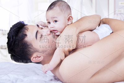 年轻的爸爸在家里亲吻他的宝宝