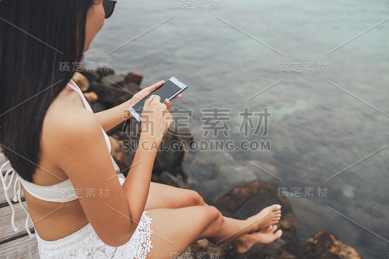 旅行者亚洲女人与手机放松在夏季的泰国海滩木桥