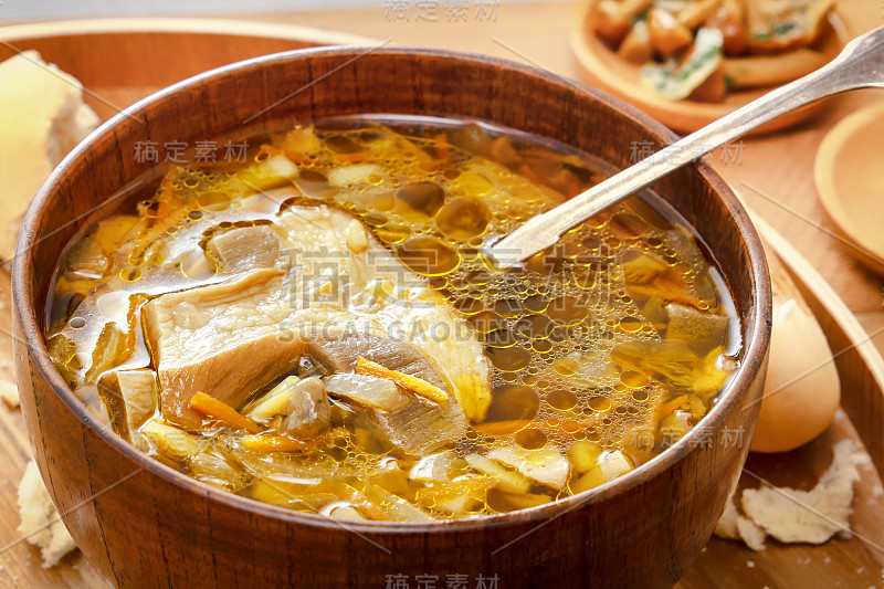 一盘蘑菇汤和一个大蘑菇。勺子放在盘子里。碎面包屑。木制背景