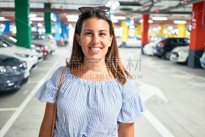 年轻女子自信地微笑在地下停车场周围的汽车和灯光
