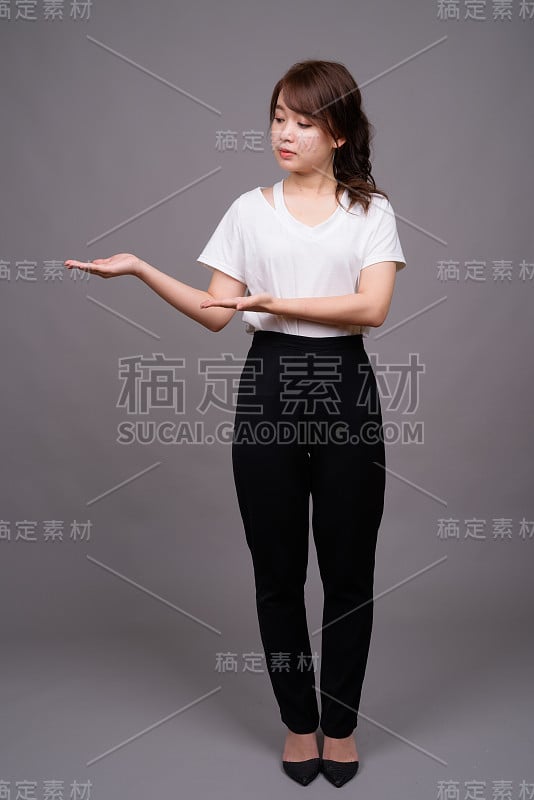 工作室拍摄的年轻美丽的亚洲妇女穿着白色衬衫，以灰色的背景