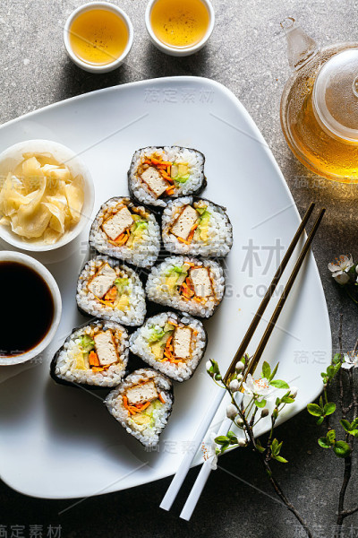 素寿司配左宗棠酱豆腐、鳄梨和新鲜蔬菜。桌子上有一棵正在开花的树的树枝，还有一个装着绿茶的玻璃茶壶
