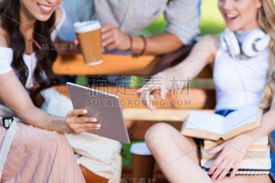 愉快的年轻学生们一起坐在公园的长凳上使用数字平板电脑