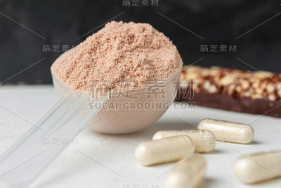 一勺乳清或大豆分离蛋白，巧克力蛋白棒，氨基酸和肌酸的白色胶囊，健身食品补充剂在白色的桌子和深色的背景
