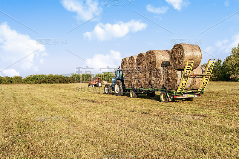 农业的场景。拖拉机在手推车上提升干草包。