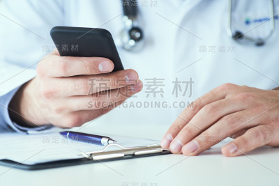 男医生手拿手机特写。一名身穿白大褂的男医生正在使用一款带有触摸屏的现代智能手机。