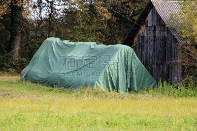 木仓旁堆放着一捆捆圆圆的干草，上面完全覆盖着厚厚的绿色尼龙，以备寒冬之用