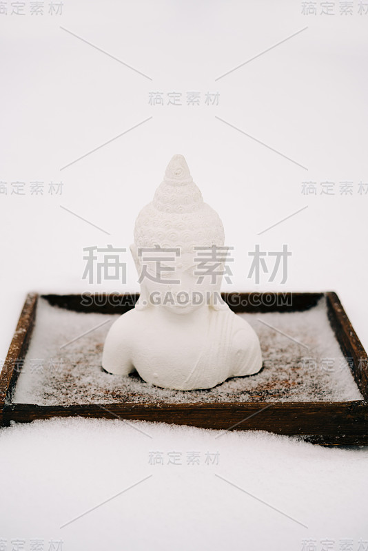 一个用石膏做成的白色小佛像，放在一个冬天下雪时覆盖着白雪的木架上