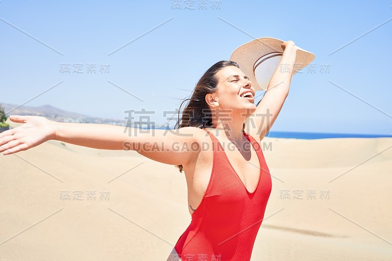 年轻美丽的女人日光浴与开放的双臂穿着夏天的swinsuit在maspalomas沙丘bech