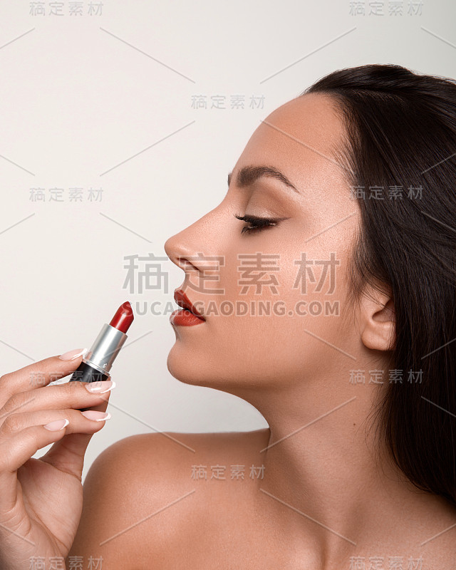 年轻漂亮的女人把红色的口红贴在嘴唇上