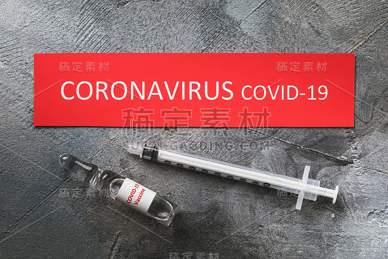 贴有铭文的标签，带有COVID-19冠状病毒疫苗的注射器和安瓿，俯视图