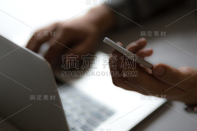 在手提电脑前拿着电话的男人