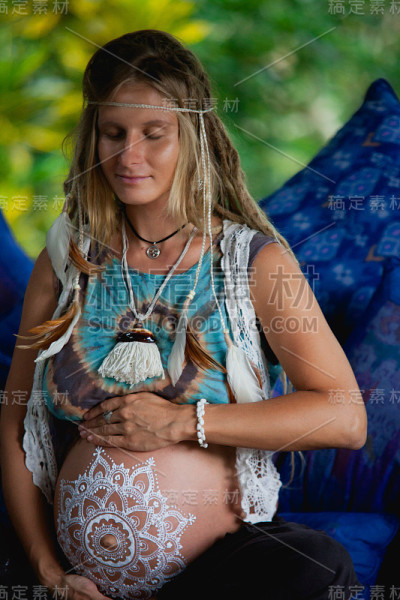 一个梳着波西米亚长发绺的白人孕妇。白色的迈赫迪在大肚子。对婴儿在新时代生活方式的期望。