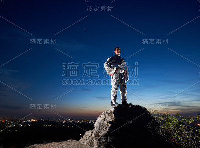 太空旅行者站在夜空下的岩石山上。
