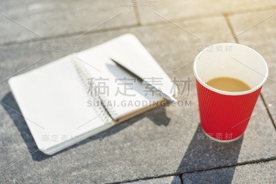 打开笔记本和空白页，钢笔和咖啡杯在灰色的铺路板上。
