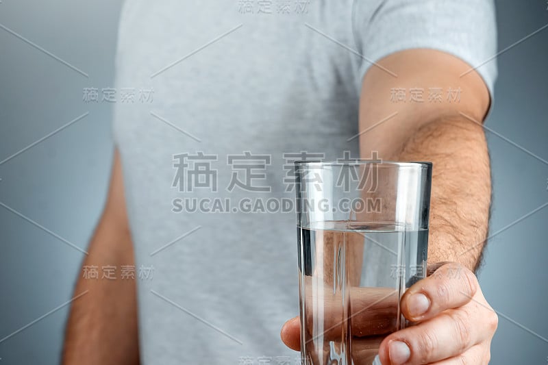 玻璃杯与纯矿泉水在男性的手特写在一个灰色的背景。药物治疗健康饮品