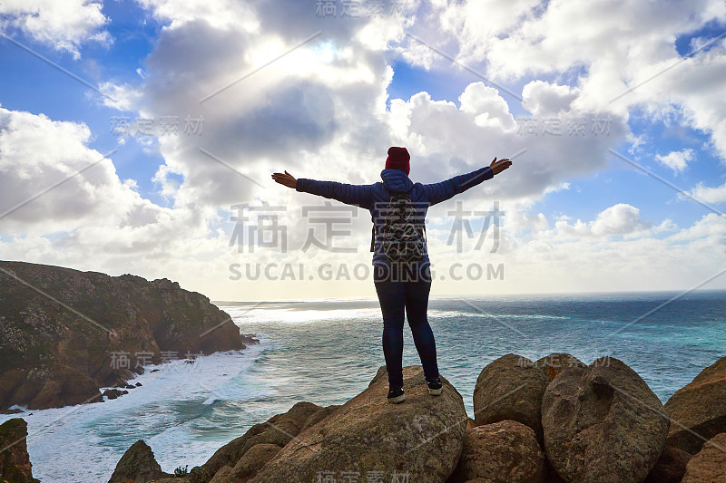 年轻的女游客站在卡波达罗卡角悬崖的岩石边缘。海浪冲击着悬崖底部的岩石