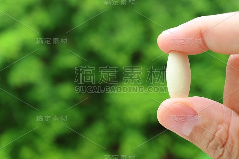 特写男子的手指拿着一个补充片对模糊的绿色树叶