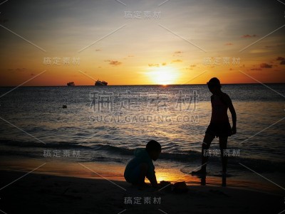 日落时，两个男孩在海滩上玩耍的剪影