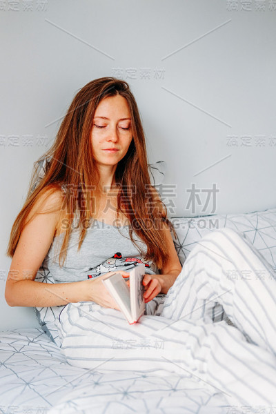 休闲时间的活动。年轻女子在床上看书。