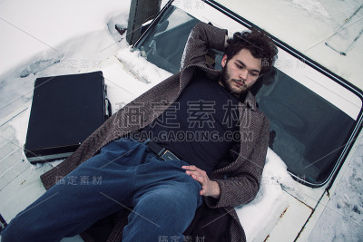 一个穿着外套的大胡子男人带着一个手提箱躺在一辆汽车上。