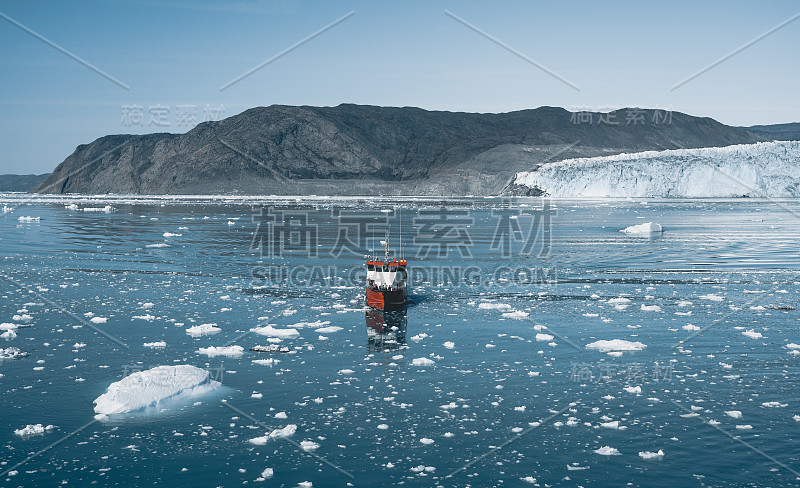 一艘红色客轮驶过格陵兰岛卡西吉安圭特的冰冷水域，背景是埃克普·塞米娅·埃奇冰川。冰山间的小船。帆船在