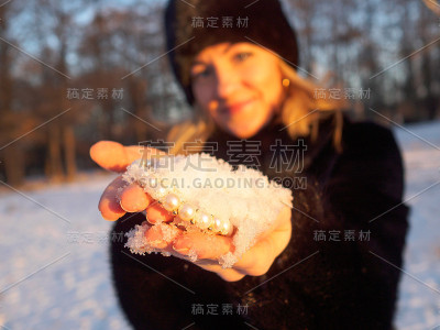 一个戴着帽子的年轻女子，手里拿着一把雪，里面是白色的珍珠首饰。