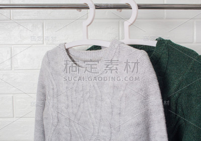 衣服挂在衣架上。毛衣是绿色和杂色的。时尚和风格，展示，商店，概念。白色砖墙，舒适和清洁，设计，舒适，
